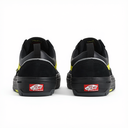 A pair of black Vans platform sneakers shown from the back, featuring a thick black sole, black suede and leather panels, and bright yellow accents on the sides and soles, with the signature red Vans logo visible on the heel.