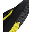Close-up of a black athletic shoe showing the side profile, textured black mesh upper, black outsole tread, and bright yellow accent panels on a white background.