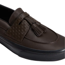 A close-up of a dark brown leather loafer with a woven strap detail and a matching tassel, shown on a plain white background.