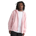 A man wearing a light pink zip-up hoodie over a white t-shirt and black pants, standing against a solid white background.