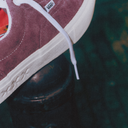 Close-up of a maroon Vans sneaker with white laces on a dark background