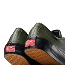 Close-up of the rear half of two Vans slip-on shoes in olive green pebbled leather with black rubber trim and tan waffle soles, showing the red 'Get the Wall' logo on the heel.