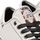 Close-up of a white Vans sneaker featuring black laces and a hockey-themed tongue patch with the Vans logo and a hockey mask graphic.