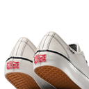 Close-up rear view of a pair of white Vans slip-on shoes showing the red Vans 'Off The Wall' logo patch on the heel, a black stripe, and a brown gum sole.