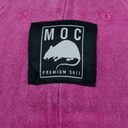 Close-up of a label with 'MOC Premium Shit' text and a rat illustration on a pink fabric background.